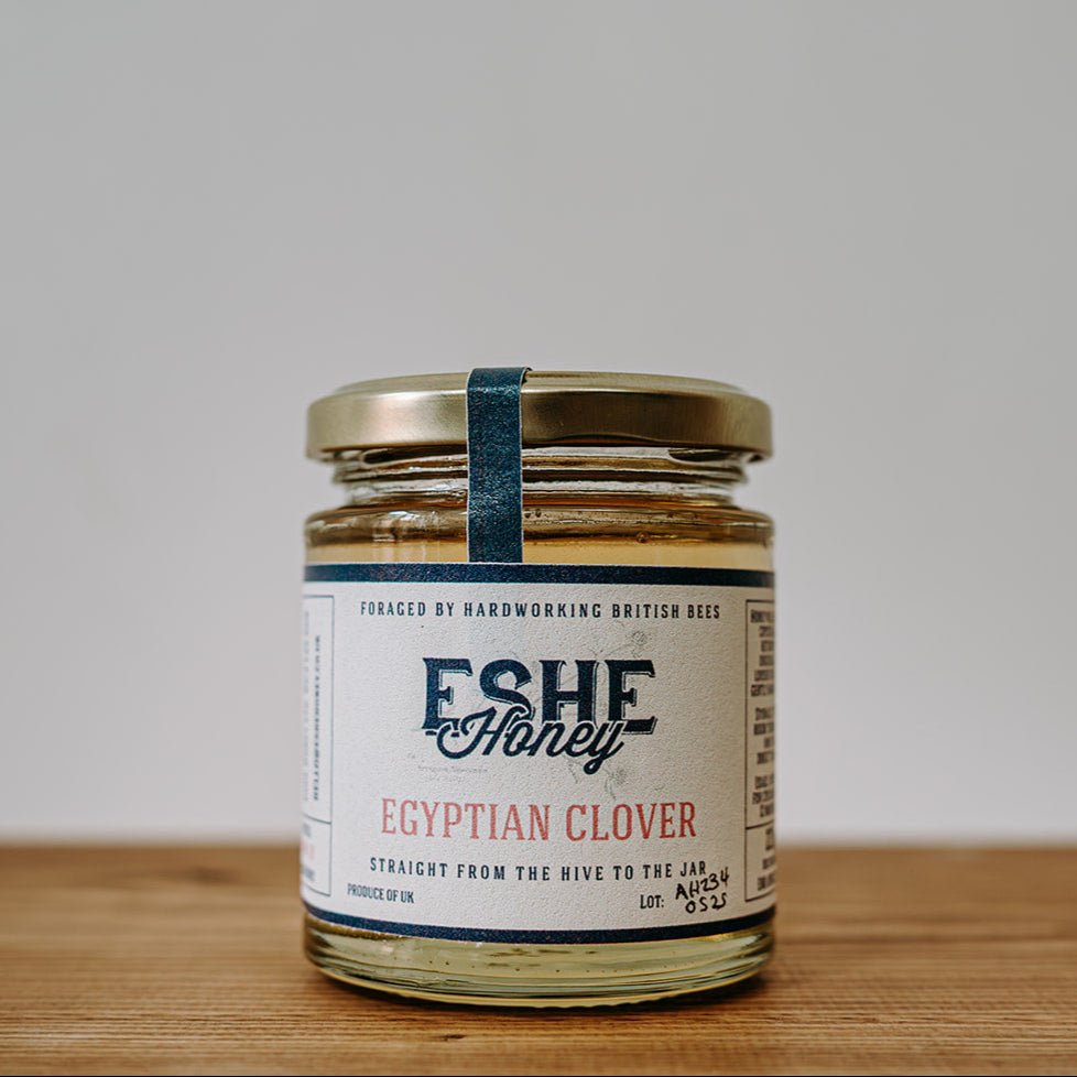 Jar of Eshe Honey Egyptian Clover on a wooden surface with a white background