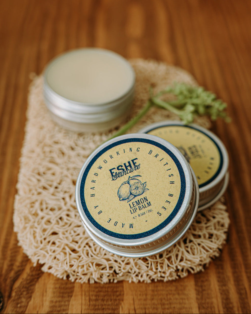 Three tins of Eshe Lemon Lip Balm on a wooden surface with a natural background.