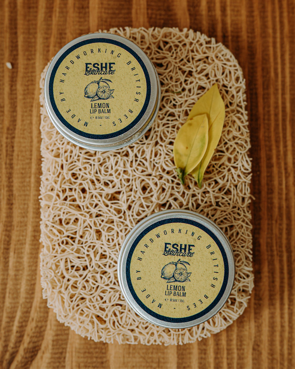 Two containers of Eshe Lemon Lip Balm on a textured surface