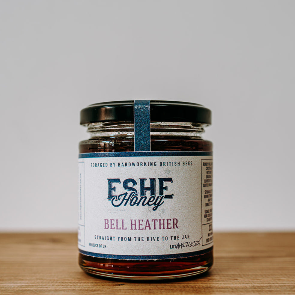Jar of Eshe Honey Bell Heather on a wooden surface with a white background