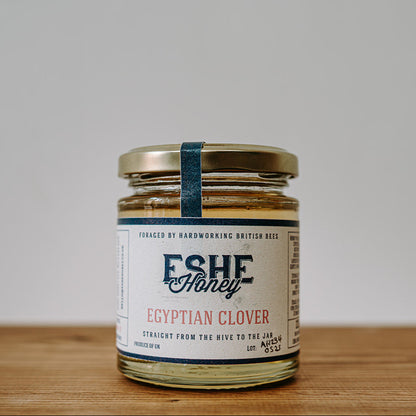 Jar of Eshe Honey Egyptian Clover on a wooden surface with a white background