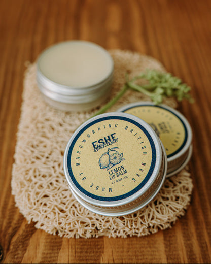 Three tins of Eshe Lemon Lip Balm on a wooden surface with a natural background.