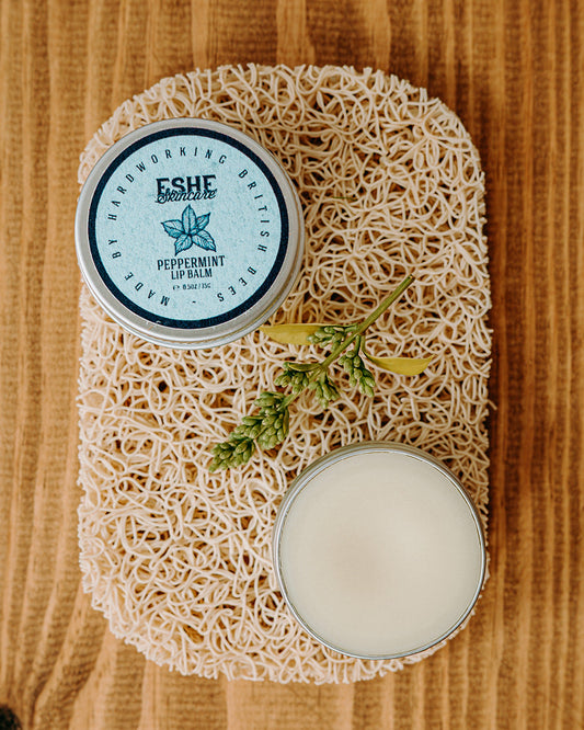 Two containers of Eshe peppermint lip balm on a wooden surface with a sponge.